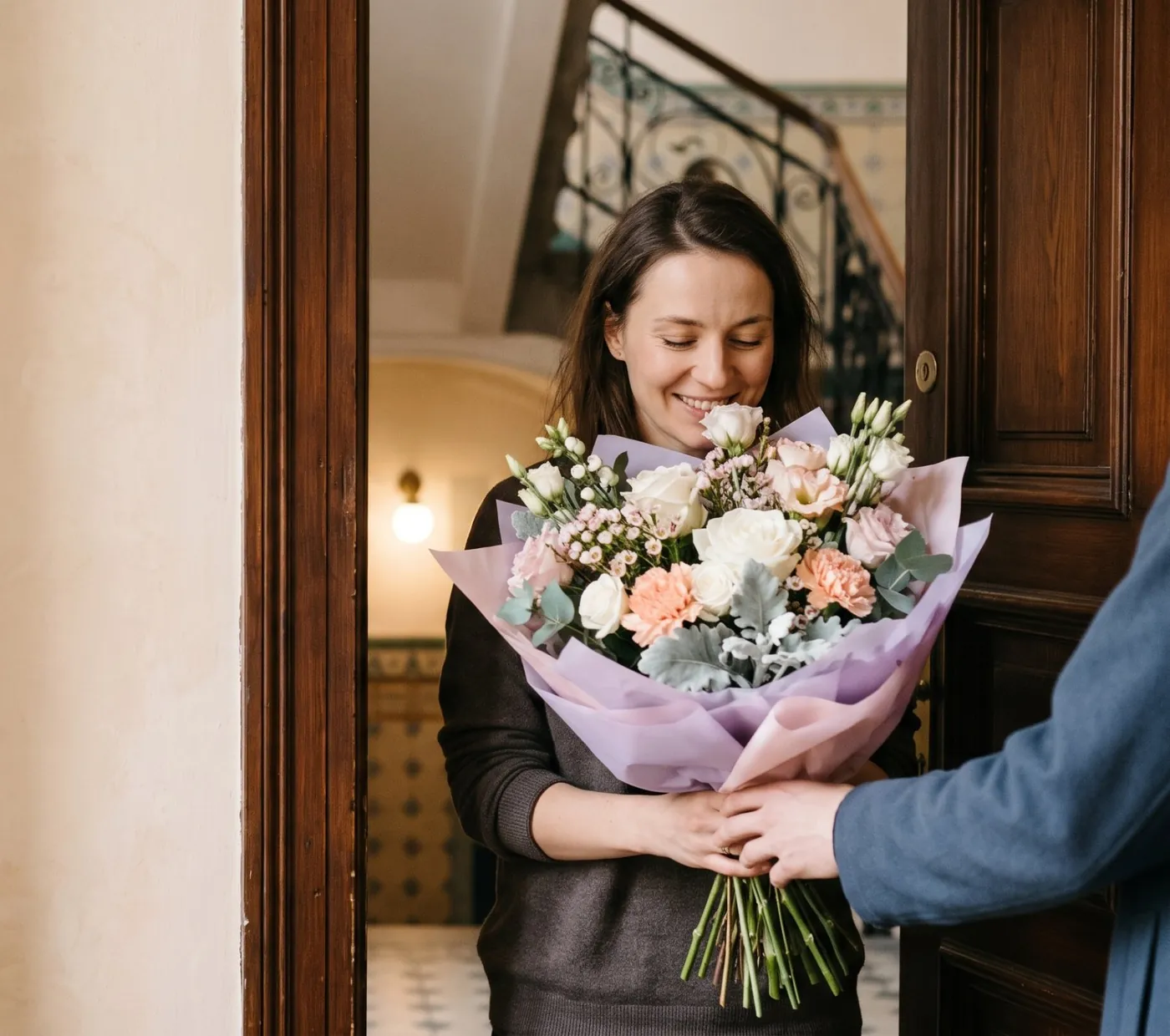A smiling woman receives a bouquet in lilac paper at the door of a Prague apartment building